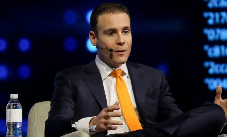 Man in suit with orange tie speaking at a conference.