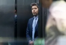 Man in suit stands in elevator, looking forward intently.