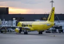 Spirit Airlines plane parked at gate D12, yellow fuselage, dusk sky.