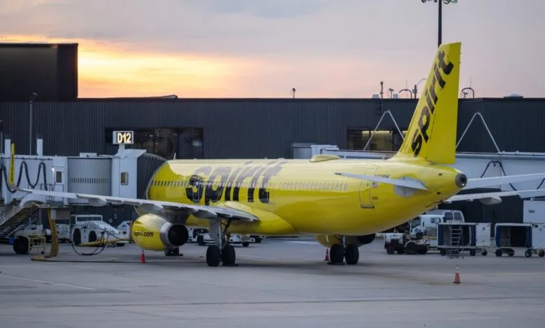 Spirit Airlines plane parked at gate D12, yellow fuselage, dusk sky.