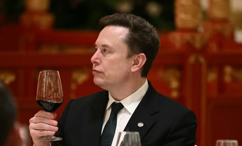 Elon Musk holds wine glass at formal dinner, looking to the side.