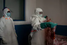 Healthcare workers in protective gear prepare isolation room.