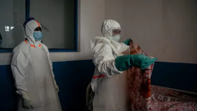 Healthcare workers in protective gear prepare isolation room.