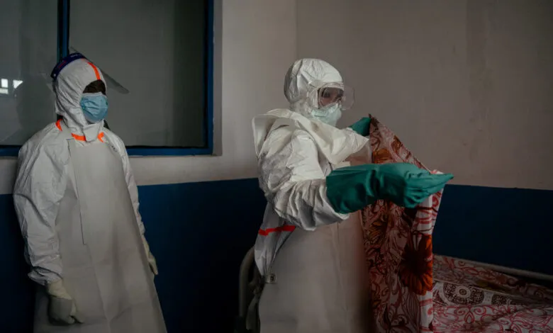 Healthcare workers in protective gear prepare isolation room.