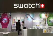 Swatch store front with colorful watches and customers inside.