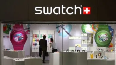 Swatch store front with colorful watches and customers inside.