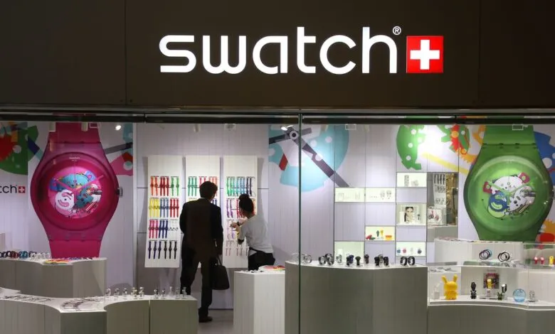 Swatch store front with colorful watches and customers inside.