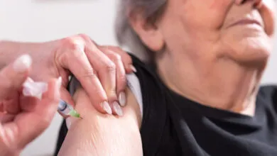Close-up of a nurse administering a vaccine to a senior woman's arm.