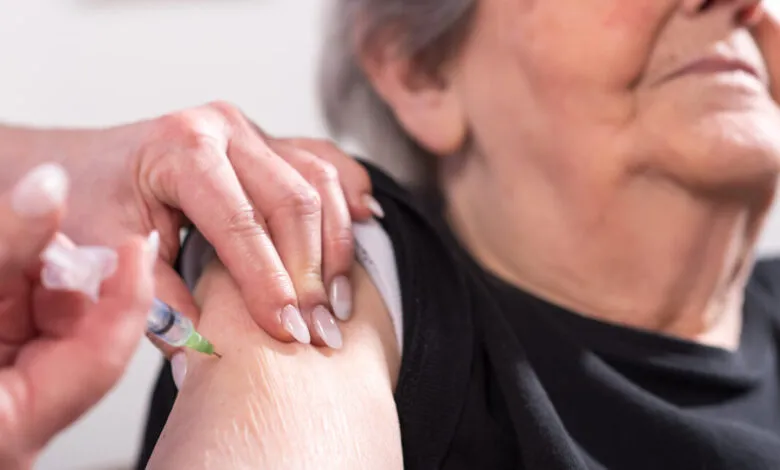 Close-up of a nurse administering a vaccine to a senior woman's arm.