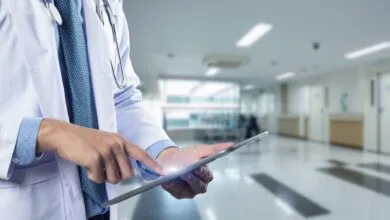 Doctor in lab coat using tablet in hospital hallway.