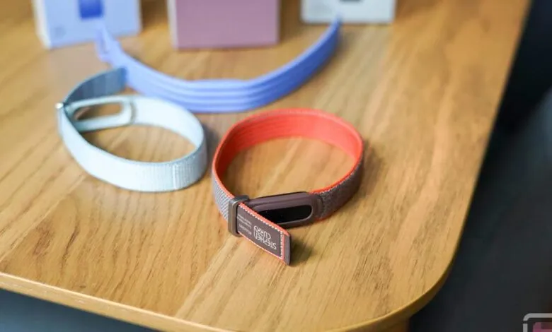 Three Fitbit bands in light blue, purple, and orange on a wooden table.
