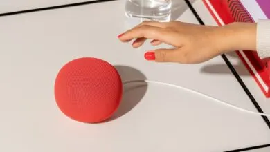 Red Google Home Mini speaker with a hand reaching towards it.