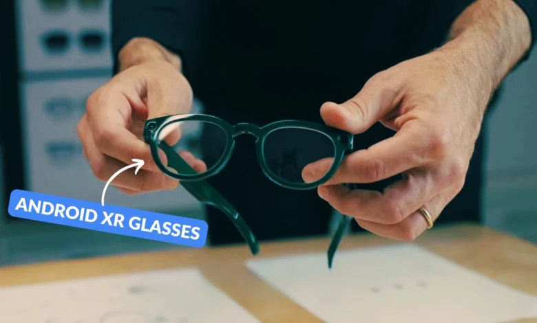 Hands holding green Android XR glasses with a small camera on the frame.