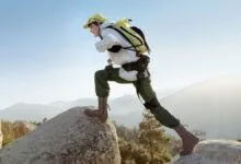 Hiker wearing exoskeleton climbs a rock with mountains in background.