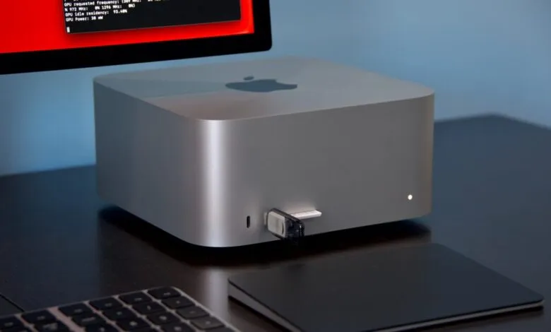 Apple Mac Studio desktop computer with USB drive plugged in, on a dark desk.