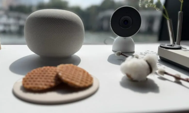 Still life with smart speaker, camera, waffles, and flowers on a white table.