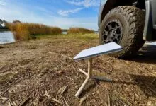 Starlink dish on stand next to vehicle tire, lakeside setting.