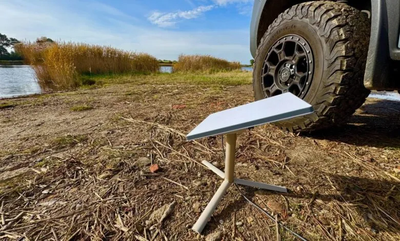 Starlink dish on stand next to vehicle tire, lakeside setting.