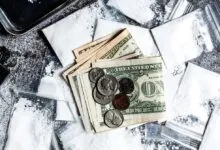 Money, bags of white powder, and a lighter on a textured surface.