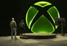 Two people stand before a large Xbox logo on a stage.
