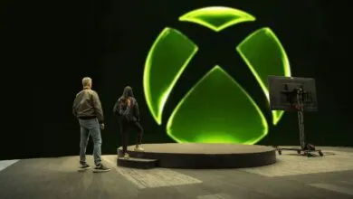 Two people stand before a large Xbox logo on a stage.