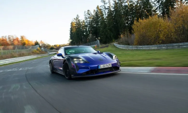 Blue Porsche Taycan Turbo GT driving on a racetrack with trees in the background.