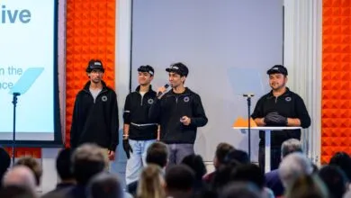 Four young entrepreneurs present on stage to an audience, wearing unique headgear.