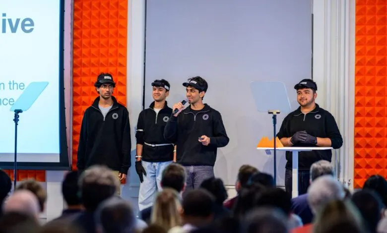 Four young entrepreneurs present on stage to an audience, wearing unique headgear.