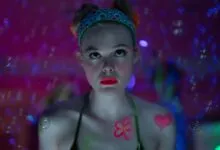Elle Fanning stares intensely with neon makeup and bubble effects.