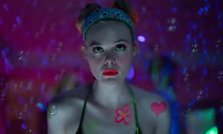 Elle Fanning stares intensely with neon makeup and bubble effects.