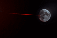 The Moon with a red laser beam pointing towards it in a dark space background.