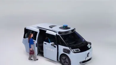 Woman exiting a light blue Waymo self-driving minivan with open door.
