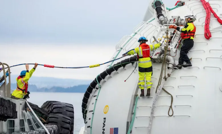Workers connect cables to a large, white ocean computing node near the water.