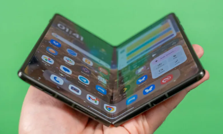 Foldable smartphone held open in hand, displaying app icons.