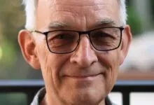 Close-up of a smiling older man with glasses and gray hair.