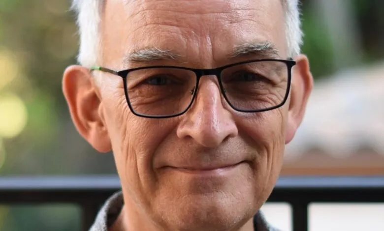 Close-up of a smiling older man with glasses and gray hair.