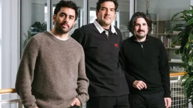 Three men stand together in a modern office setting, posing for a photo.