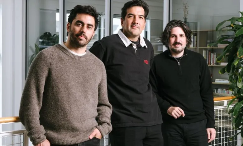 Three men stand together in a modern office setting, posing for a photo.