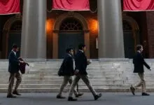 Four students walk in front of a building with large columns and red banners.