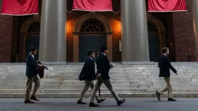 Four students walk in front of a building with large columns and red banners.