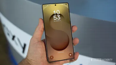 Hand holding a Samsung Galaxy S25 Ultra phone with a gold and brown abstract wallpaper.