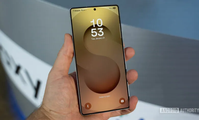Hand holding a Samsung Galaxy S25 Ultra phone with a gold and brown abstract wallpaper.