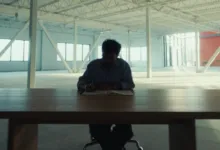 Man writing in notebook at large wooden table in empty warehouse.