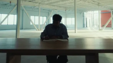 Man writing in notebook at large wooden table in empty warehouse.