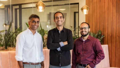 Three smiling men pose indoors with modern decor and warm lighting.