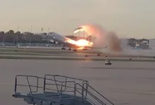 Airplane engulfed in flames takes off from runway, smoke billowing behind.