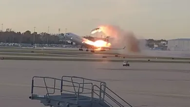 Airplane engulfed in flames takes off from runway, smoke billowing behind.