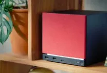 Red and black cube-shaped computer on a wooden shelf.