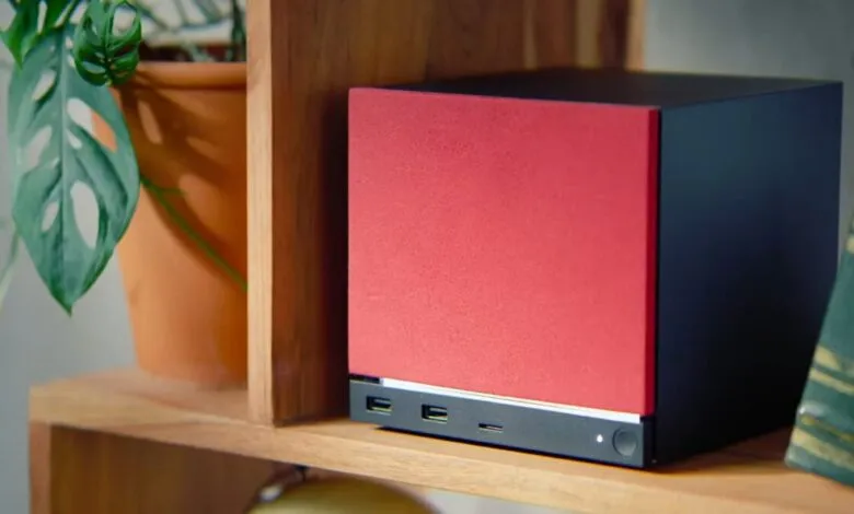 Red and black cube-shaped computer on a wooden shelf.