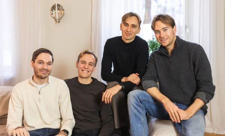 Four young men pose on a couch in a bright, modern living room.